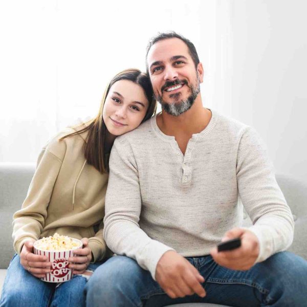 father and teen girl watching television while eating pop corn at home